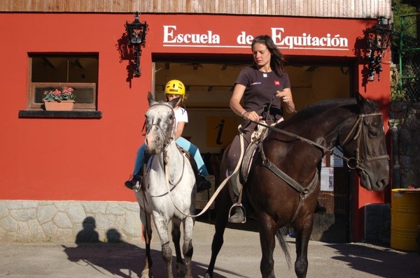 Niña montando un pony blanco guiada por una instructora frente a la Escuela de Equitación en el Valle de Arán